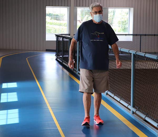Older gentleman walks on an upper blue track in shorts and a shirt.