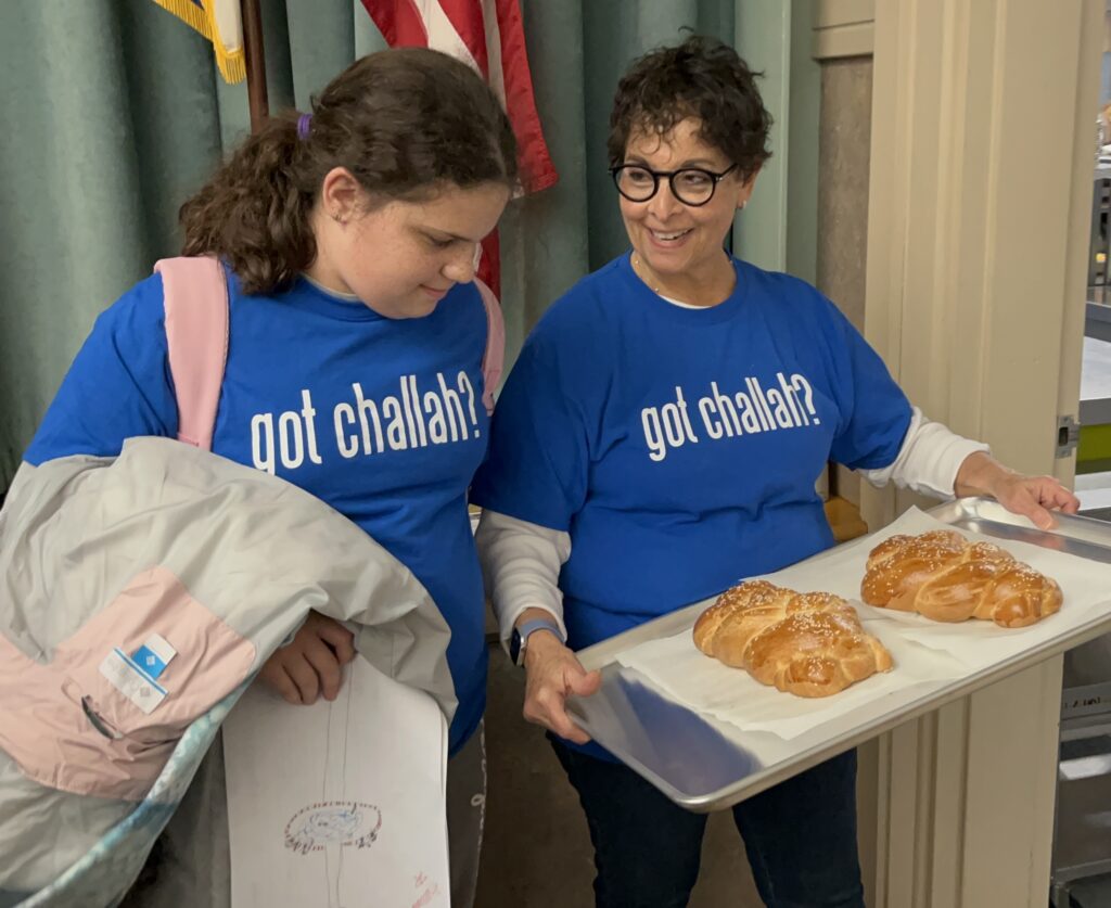 Women and young girl looking at their recently made challah bread in 'got challah' shirts
