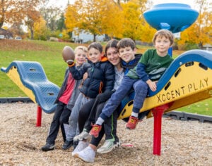 group of children sitting on playground equipment with teacher